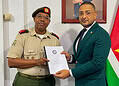 Dissertation presentation beside Suriname flag El teniente coronel Vernon W. Pengel propone reforzar la Ley de Aplicación de la Convención sobre Armas Químicas, con miras a mejores posibilidades de supervisión para la Suriname Non-proliferatie Autoriteit (Autoridad de No Proliferación de Surinam).