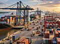 Deep-water port in Berbice: major US$ 2 billion project in 2026 2 Busy shipping port with cargo ships docked under tall cranes, surrounded by stacked containers and trucks at sunset