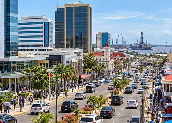 Centre-ville de Georgetown, Guyana, avec des immeubles, une avenue animée bordée de palmiers, des piétons, de la circulation et le port avec des navires en arrière-plan